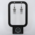 Handmade stainless steel chainmail earrings with a centre bead, side spikes and twin spike drops, displayed on a black earring stand against a light background.