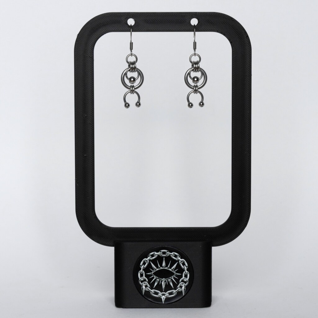 Handmade stainless steel earrings with an open circle ring and a curved horseshoe arc with bead ends, displayed on a black earring stand against a light background.