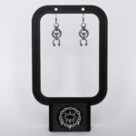 Handmade stainless steel earrings with an open circle ring and a curved horseshoe arc with bead ends, displayed on a black earring stand against a light background.