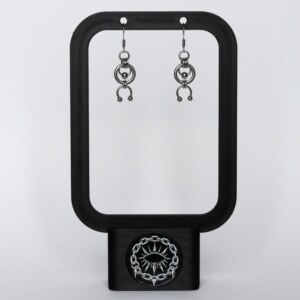 Handmade stainless steel earrings with an open circle ring and a curved horseshoe arc with bead ends, displayed on a black earring stand against a light background.