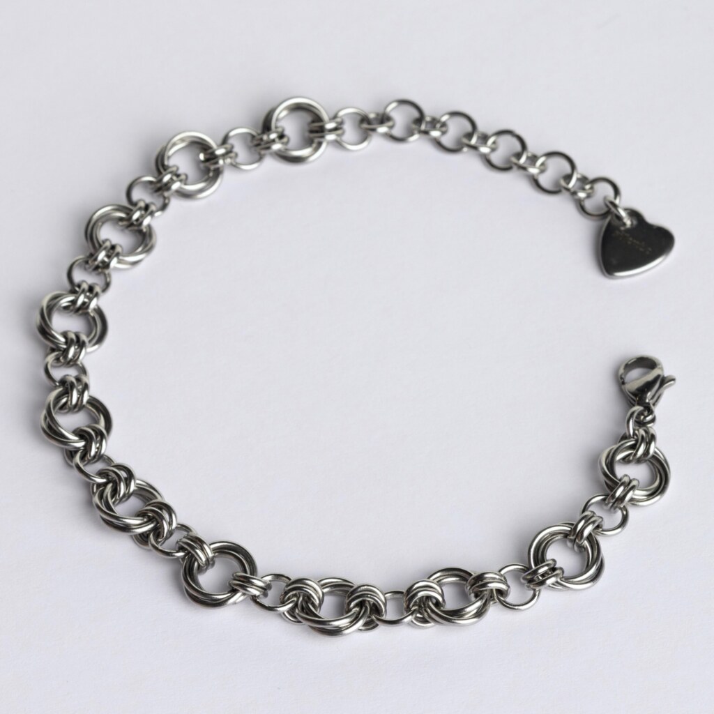 Handmade stainless steel chainmail bracelet with a dense Helm weave, lobster clasp and silentchxos heart tag, photographed flat against a light background.