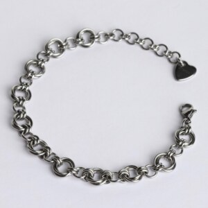 Handmade stainless steel chainmail bracelet with a dense Helm weave, lobster clasp and silentchxos heart tag, photographed flat against a light background.