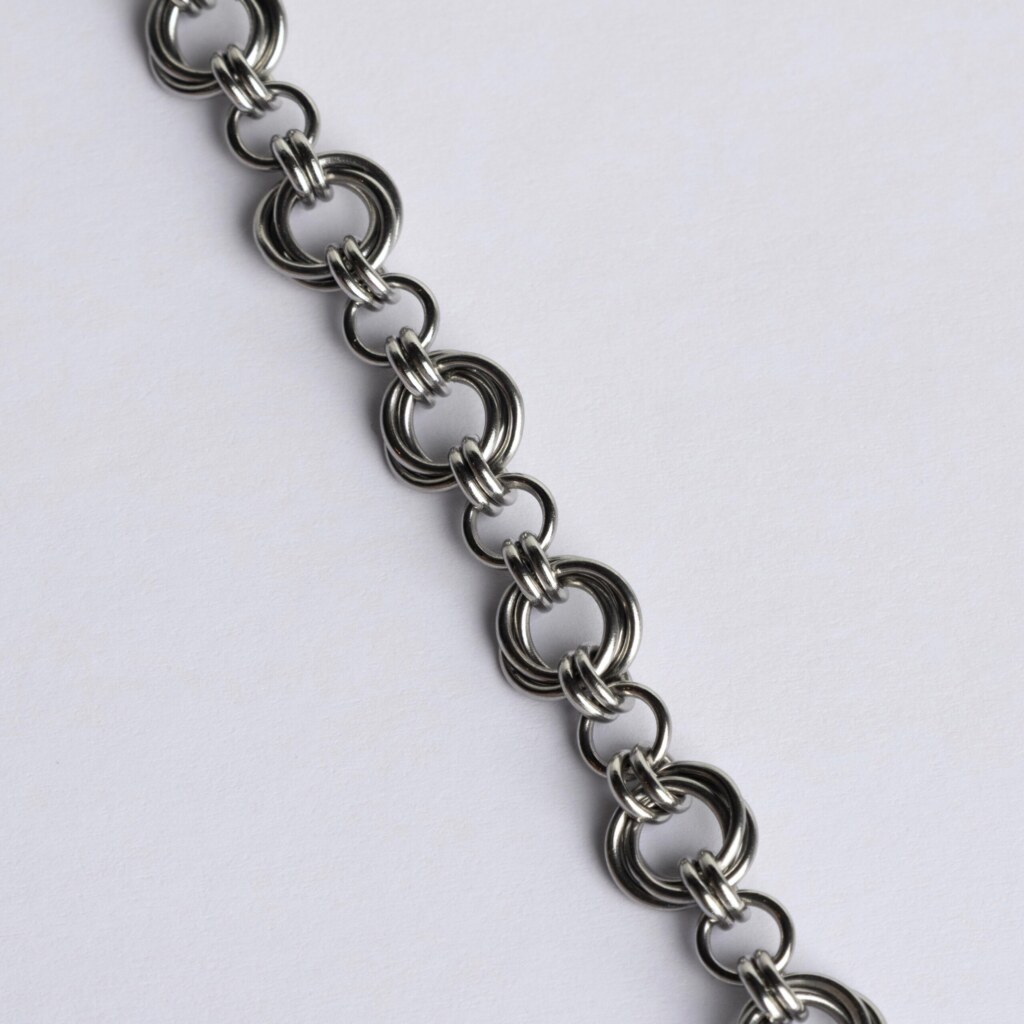 Close-up of a handmade stainless steel chainmail bracelet showing the detailed Helm weave pattern with interlocking large and small rings.