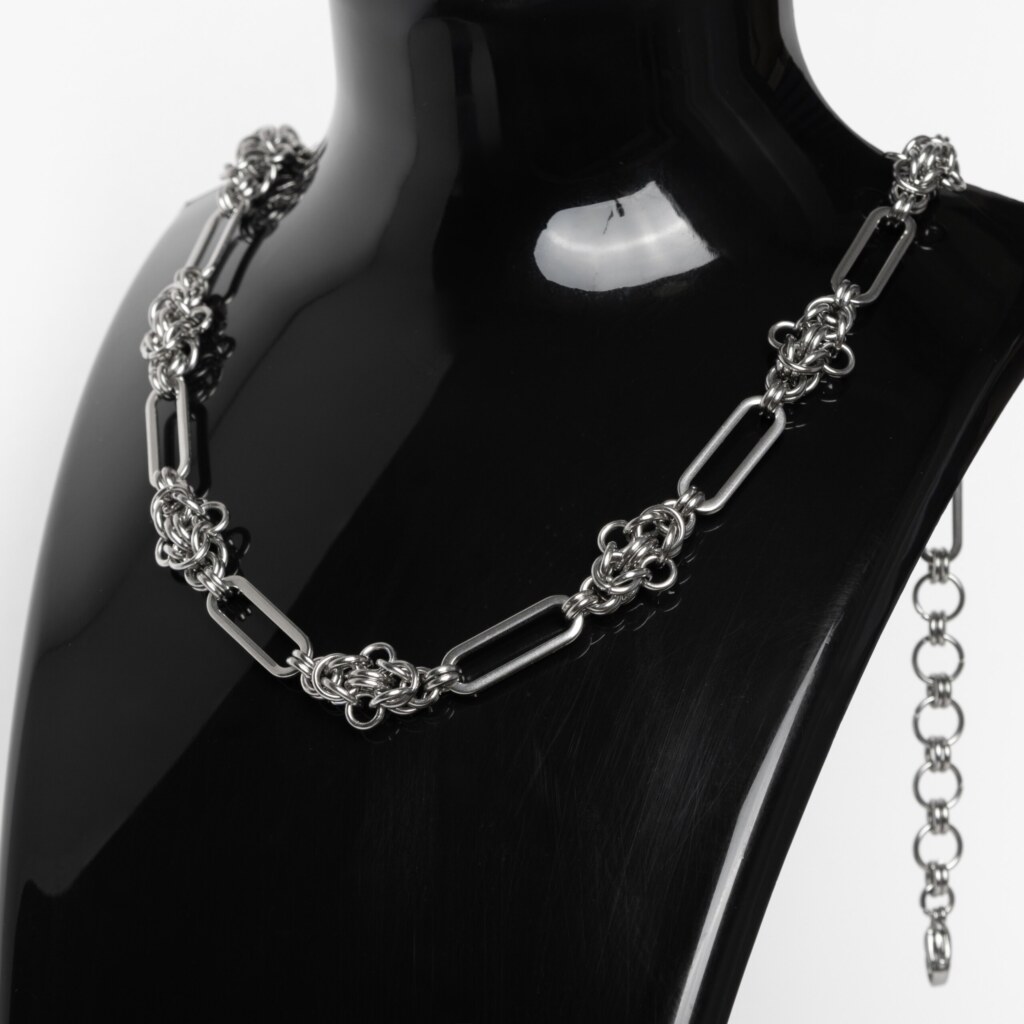 Handmade stainless steel chainmail necklace with alternating elongated oval links and dense compact woven knot units, displayed against a neutral background.