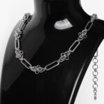 Handmade stainless steel chainmail necklace with alternating elongated oval links and dense compact woven knot units, displayed against a neutral background.