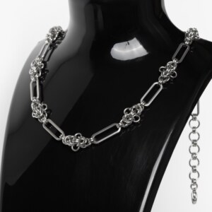 Handmade stainless steel chainmail necklace with alternating elongated oval links and dense compact woven knot units, displayed against a neutral background.