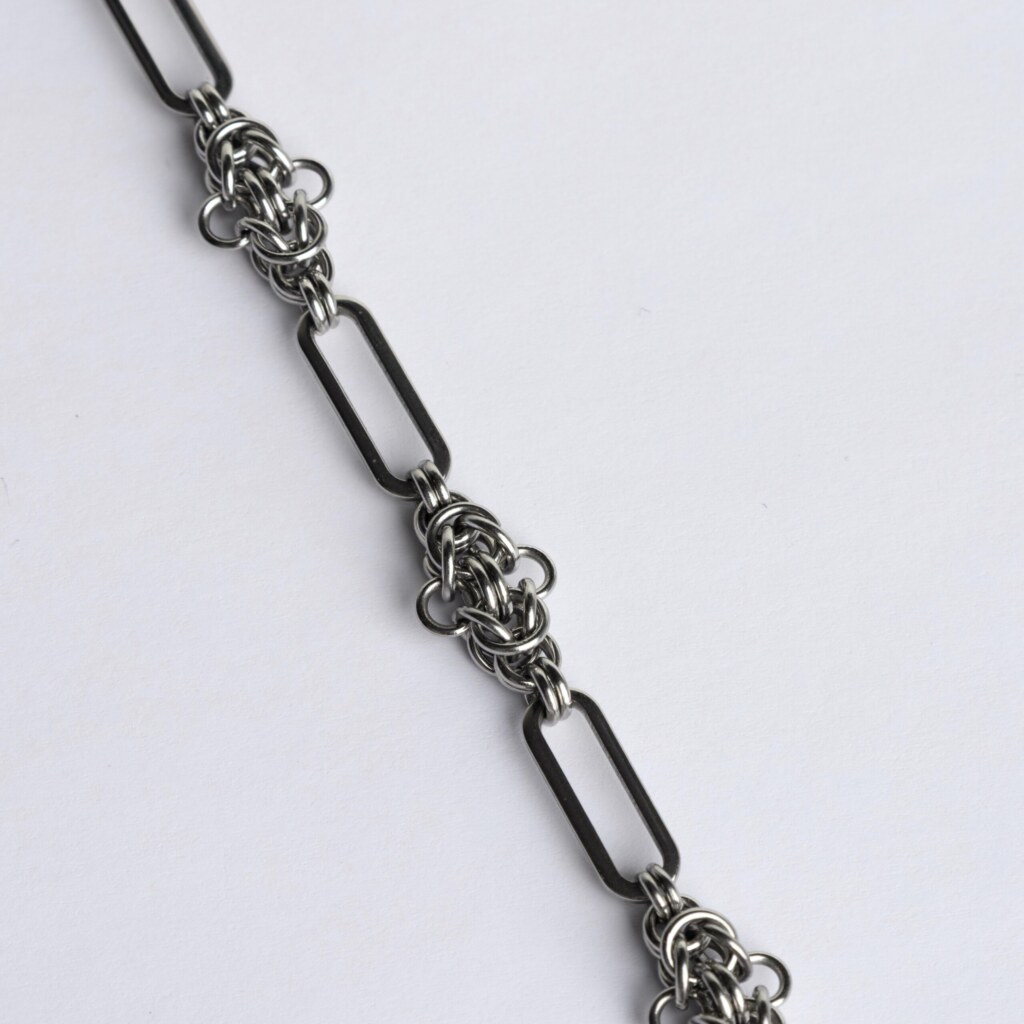 Close-up of a handmade stainless steel chainmail necklace showing alternating elongated oval links and tightly woven compact chainmail knot units.