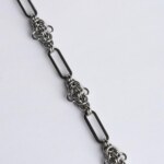 Close-up of a handmade stainless steel chainmail necklace showing alternating elongated oval links and tightly woven compact chainmail knot units.