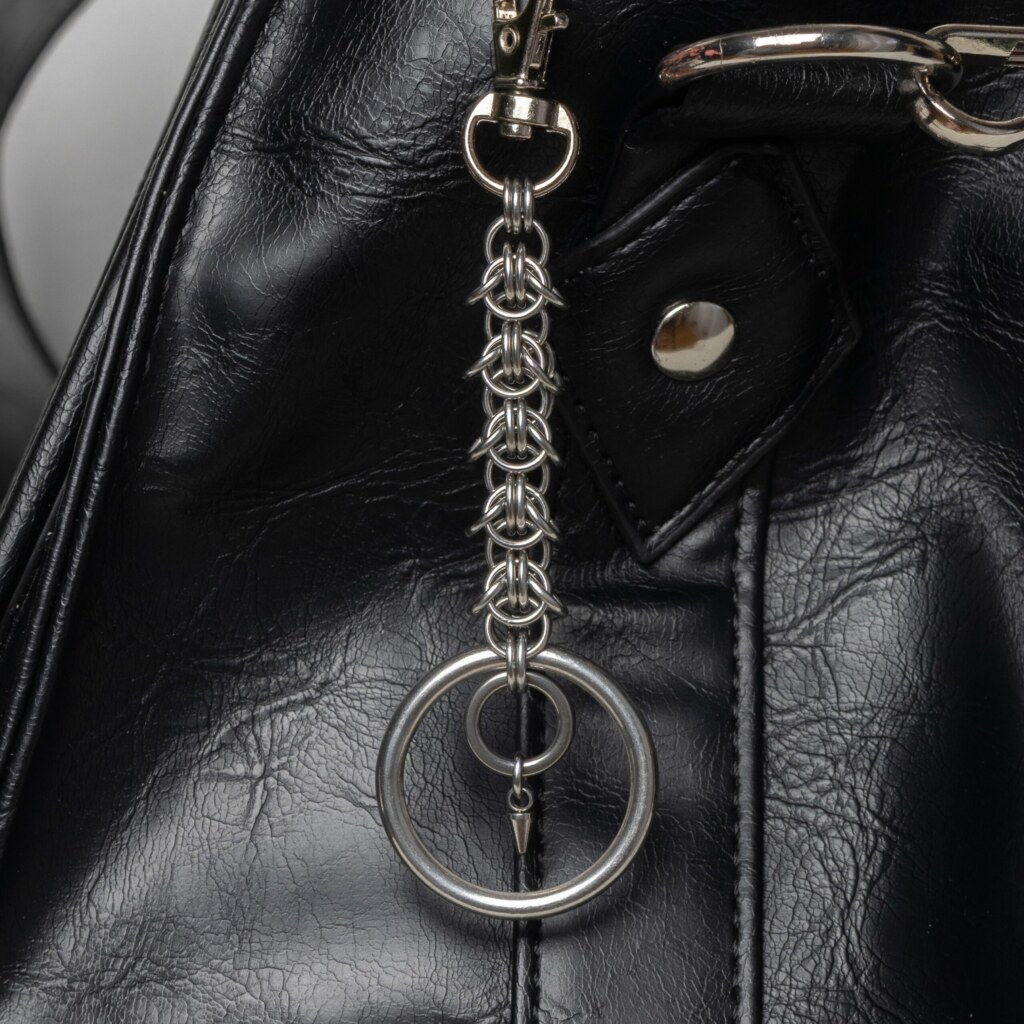 Handmade stainless steel chainmail keychain with a woven chainmail segment, large key ring and small spike drop, attached to a black bag.