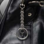 Handmade stainless steel chainmail keychain with a woven chainmail segment, large key ring and small spike drop, attached to a black bag.