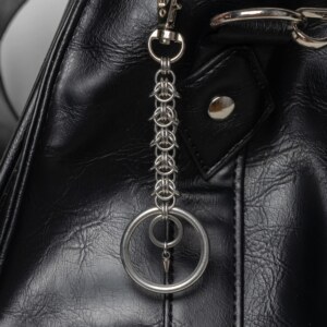 Handmade stainless steel chainmail keychain with a woven chainmail segment, large key ring and small spike drop, attached to a black bag.