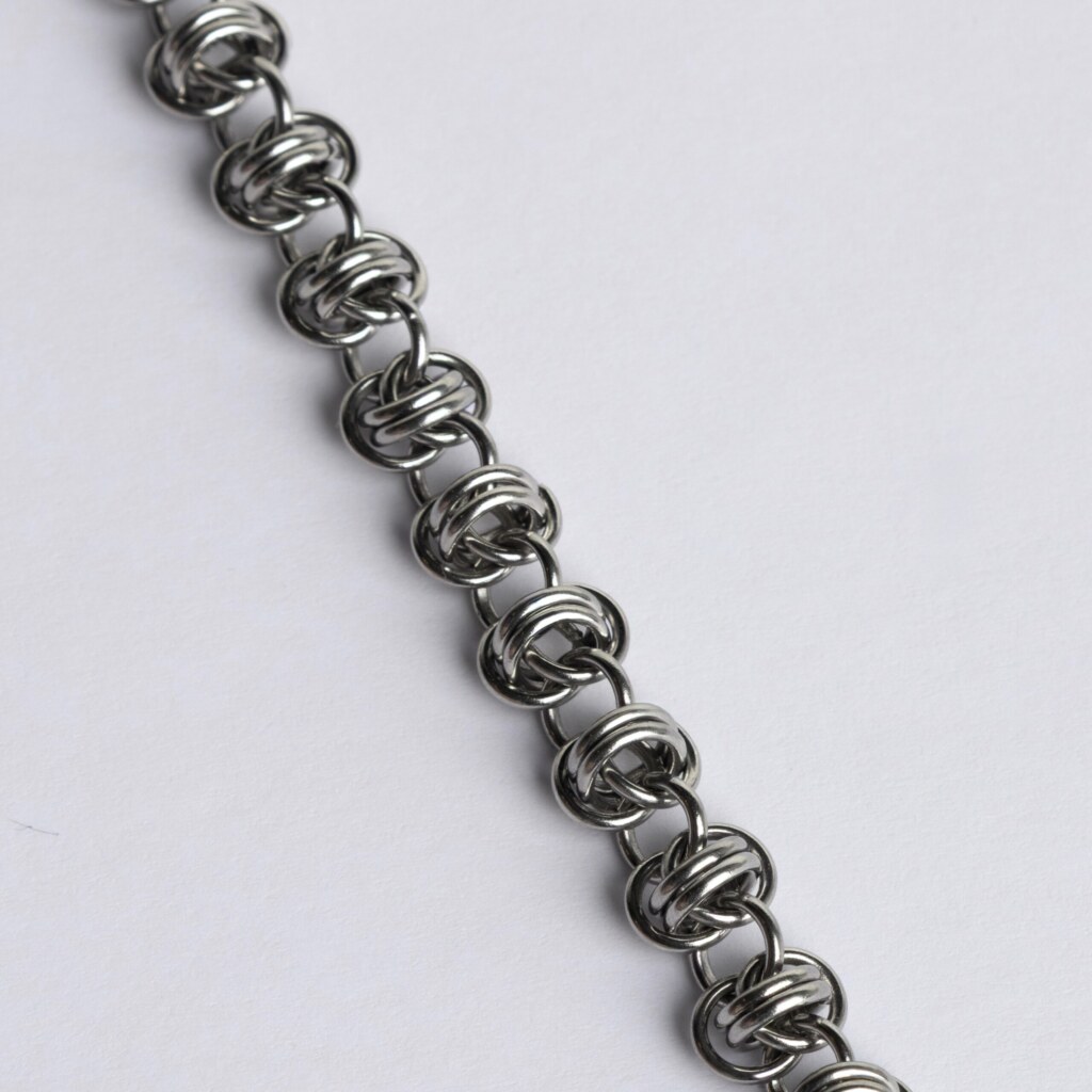 Close-up of a handmade stainless steel chainmail bracelet showing a wild, knotted weave with tightly interlocked rings.