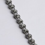 Close-up of a handmade stainless steel chainmail bracelet showing a wild, knotted weave with tightly interlocked rings.