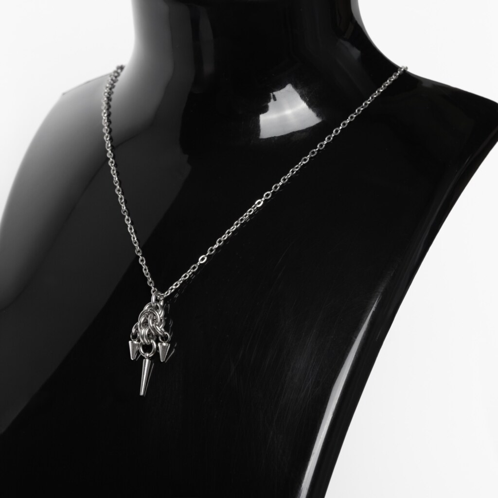 Close-up of a handmade stainless steel minimalist necklace with a chainmail knot and three small spike pendants hanging from a fine cable chain.