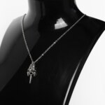 Close-up of a handmade stainless steel minimalist necklace with a chainmail knot and three small spike pendants hanging from a fine cable chain.