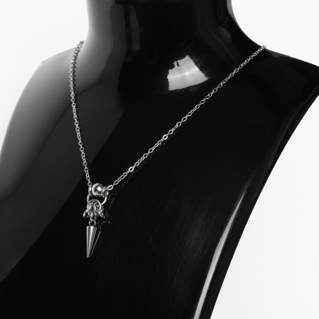 Close-up of a handmade stainless steel minimalist necklace with a large bead, chainmail knot and single elongated spike pendant on a fine cable chain.