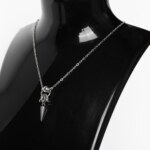 Close-up of a handmade stainless steel minimalist necklace with a large bead, chainmail knot and single elongated spike pendant on a fine cable chain.