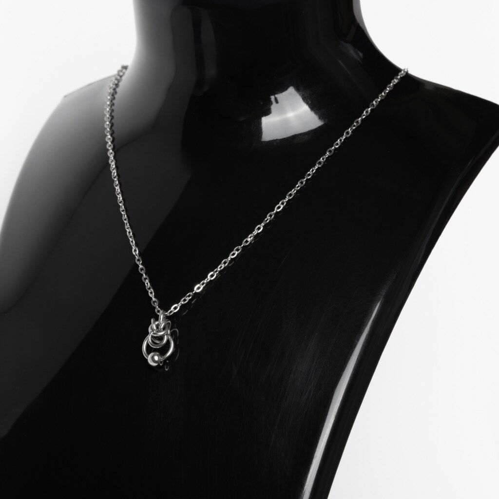 Close-up of a handmade stainless steel minimalist necklace with a small chainmail knot, open ring and bead pendant on a fine cable chain.