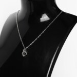 Close-up of a handmade stainless steel minimalist necklace with a small chainmail knot, open ring and bead pendant on a fine cable chain.