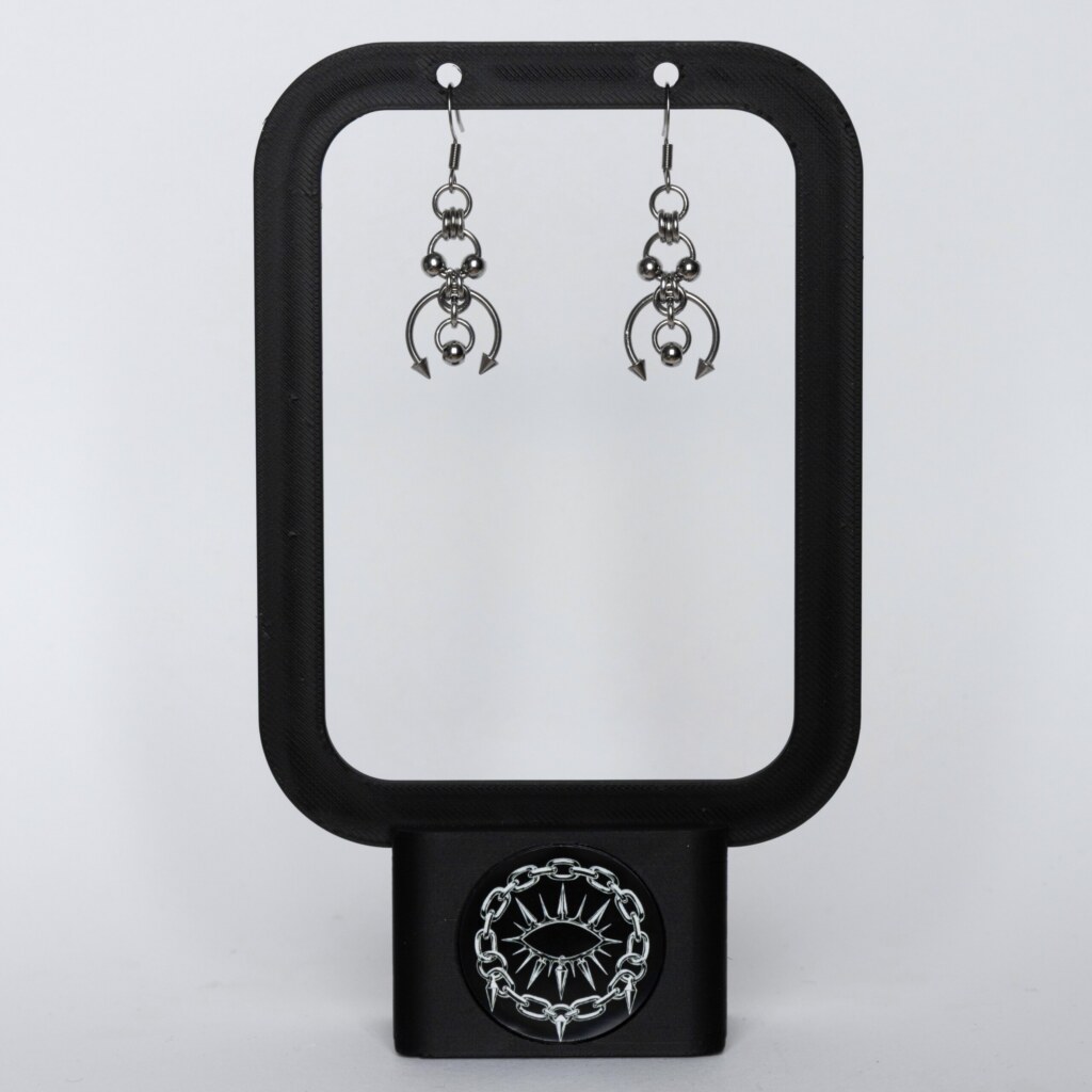 Handmade stainless steel earrings with layered bead details, an open horseshoe ring and twin spike ends, displayed on a black earring stand against a light background.