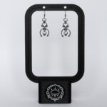 Handmade stainless steel earrings with layered bead details, an open horseshoe ring and twin spike ends, displayed on a black earring stand against a light background.