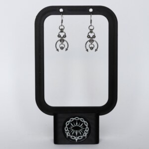 Handmade stainless steel earrings with layered bead details, an open horseshoe ring and twin spike ends, displayed on a black earring stand against a light background.