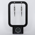 Handmade stainless steel chainmail spike earrings with elongated spike drop, displayed on a black earring stand against a light background.