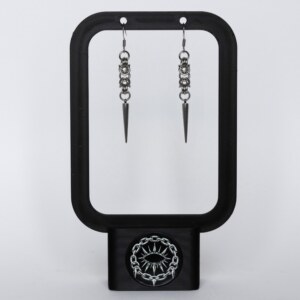 Handmade stainless steel chainmail spike earrings with elongated spike drop, displayed on a black earring stand against a light background.