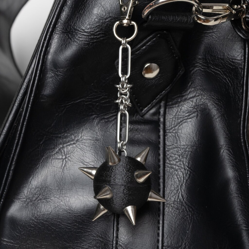 Handmade bag charm with a black spiked ball pendant and stainless steel paperclip chain, attached to a black leather bag.