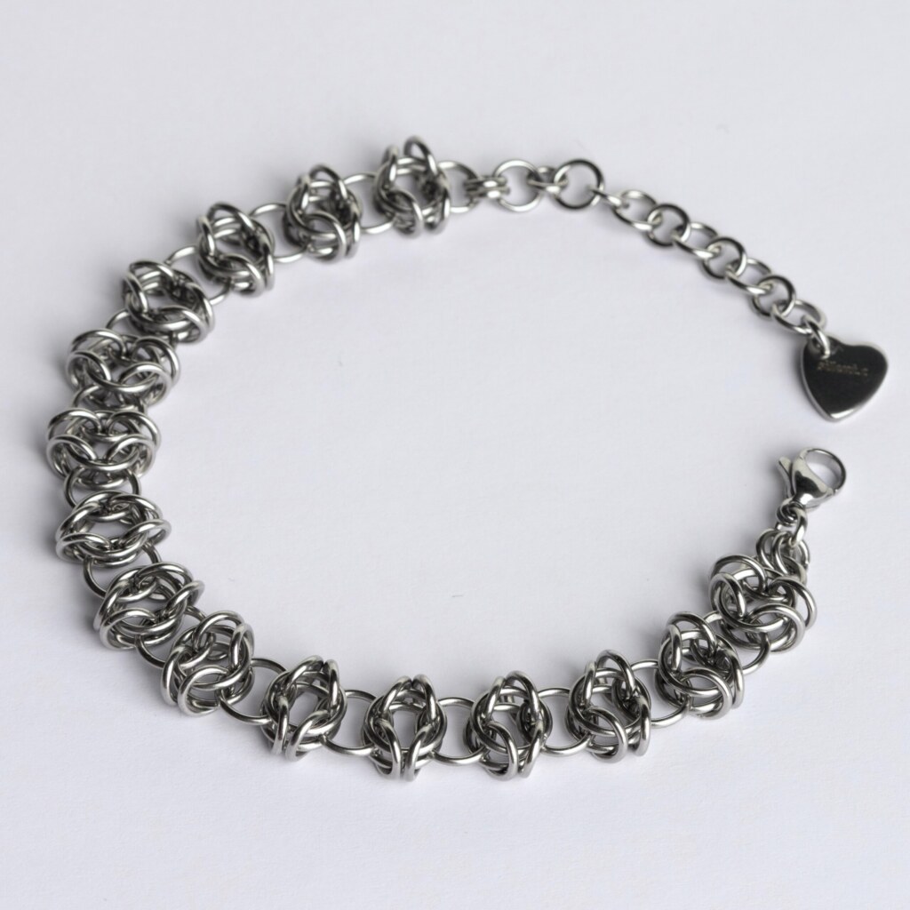 Handmade stainless steel chainmail bracelet with an open oval-link weave pattern, lobster clasp, extension chain and silentchxos heart tag, photographed flat against a light background.