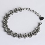 Handmade stainless steel chainmail bracelet with an open oval-link weave pattern, lobster clasp, extension chain and silentchxos heart tag, photographed flat against a light background.
