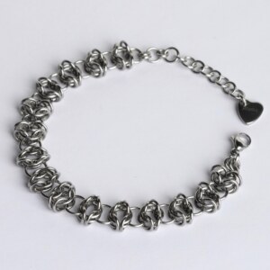 Handmade stainless steel chainmail bracelet with an open oval-link weave pattern, lobster clasp, extension chain and silentchxos heart tag, photographed flat against a light background.