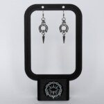 Handmade stainless steel earrings featuring a large open circle ring with bead details and a spike drop, displayed on a black earring stand against a light background.