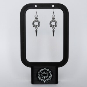 Handmade stainless steel earrings featuring a large open circle ring with bead details and a spike drop, displayed on a black earring stand against a light background.