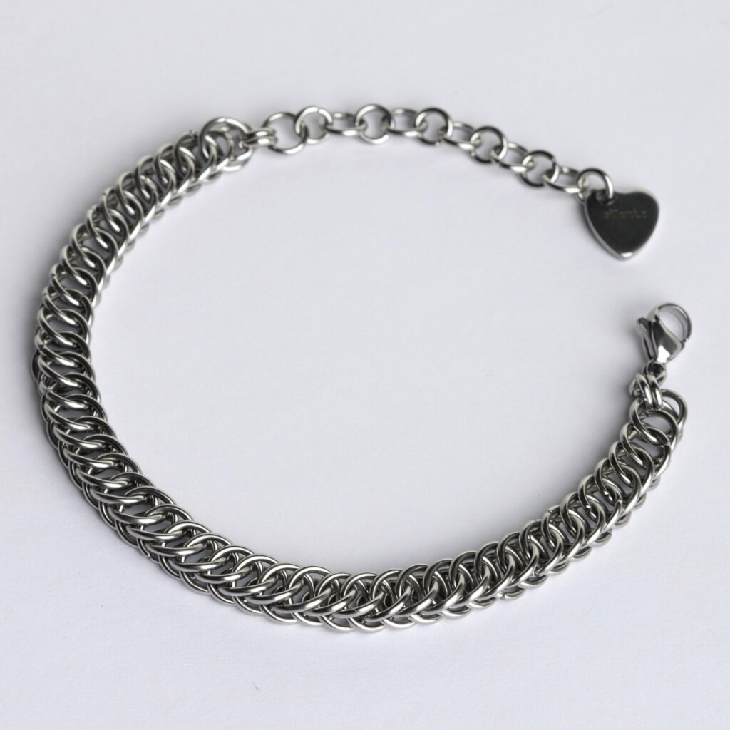 Handmade stainless steel chainmail bracelet with a flat scale-pattern Half Persian weave, lobster clasp, extension chain and silentchxos heart tag, photographed flat against a light background.