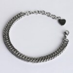 Handmade stainless steel chainmail bracelet with a flat scale-pattern Half Persian weave, lobster clasp, extension chain and silentchxos heart tag, photographed flat against a light background.