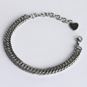 Handmade stainless steel chainmail bracelet with a flat scale-pattern Half Persian weave, lobster clasp, extension chain and silentchxos heart tag, photographed flat against a light background.