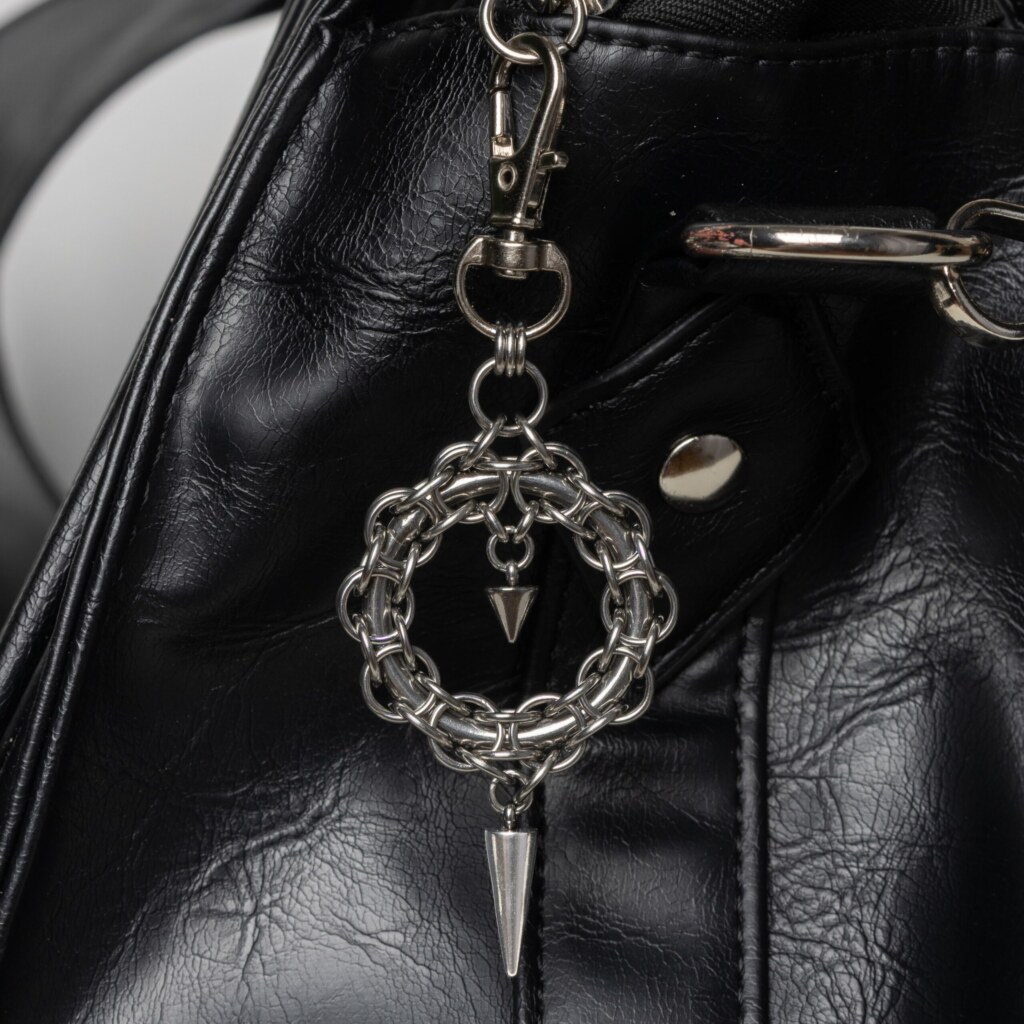 Handmade stainless steel chainmail wreath charm with inner spike and long spike drop, attached to a black bag.