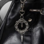 Handmade stainless steel chainmail wreath charm with inner spike and long spike drop, attached to a black bag.