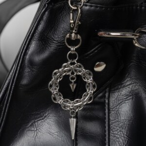 Handmade stainless steel chainmail wreath charm with inner spike and long spike drop, attached to a black bag.
