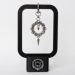 Handmade stainless steel chainmail wreath keychain charm with small inner spike and elongated spike drop on a swivel clasp, displayed on a black stand against a light background.