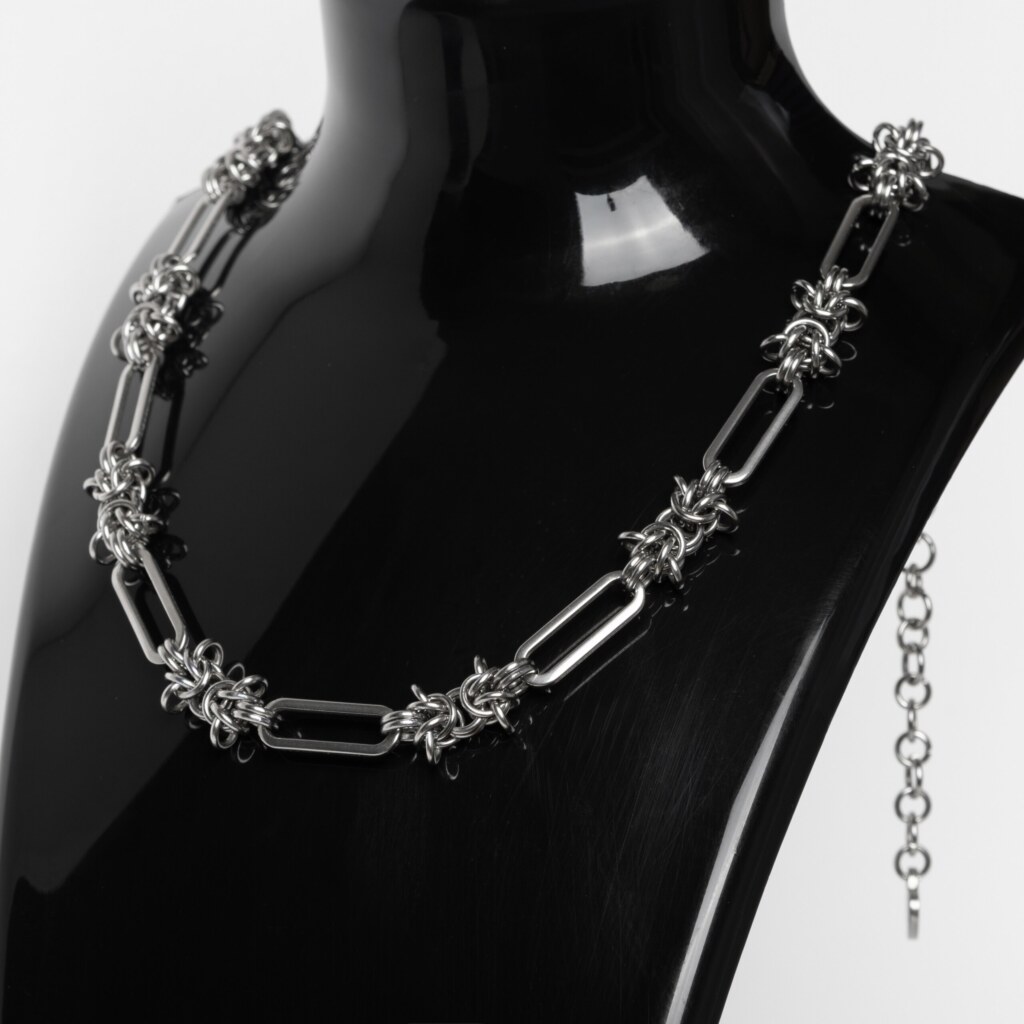 Handmade stainless steel chainmail necklace with alternating elongated oval links and woven knot units, displayed against a neutral background.