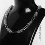 Handmade stainless steel chainmail necklace with alternating elongated oval links and woven knot units, displayed against a neutral background.