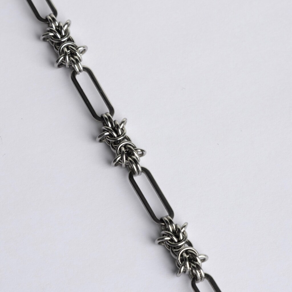 Close-up of a handmade stainless steel chainmail necklace showing alternating elongated oval links and dense woven chainmail knot units.