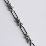 Close-up of a handmade stainless steel chainmail necklace showing alternating elongated oval links and dense woven chainmail knot units.
