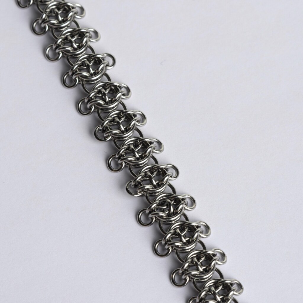 Close-up of a handmade stainless steel chainmail bracelet showing a three-dimensional weave pattern with small rings extending outward from each central link unit.