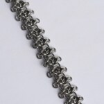 Close-up of a handmade stainless steel chainmail bracelet showing a three-dimensional weave pattern with small rings extending outward from each central link unit.