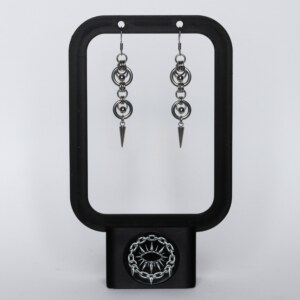 Handmade stainless steel chainmail earrings with repeating ring and bead links leading to a long spike drop, displayed on a black earring stand against a light background.