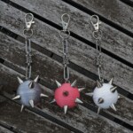 Handmade bag charm with a spiked ball pendant and stainless steel paperclip chain in different colors, lying on an table.