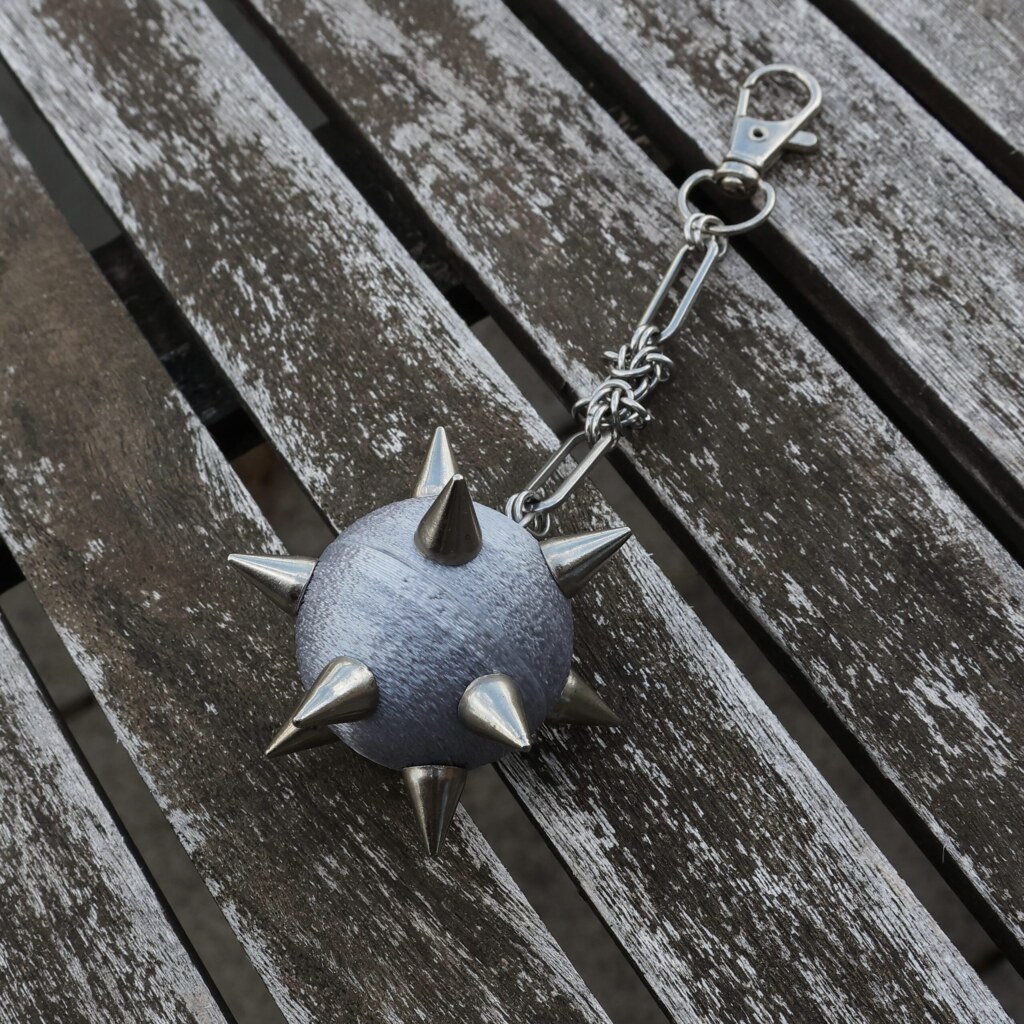 Handmade bag charm with a silver spiked ball pendant and stainless steel paperclip chain, lying on an table.